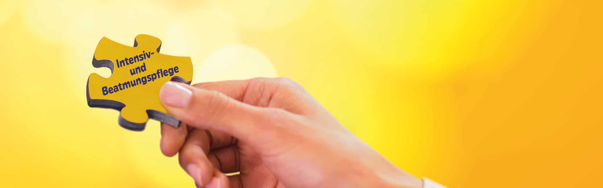 Hand hält ein gelbes Puzzle mit der Aufschrift ‚Intensiv- und Beatmungspflege‘.