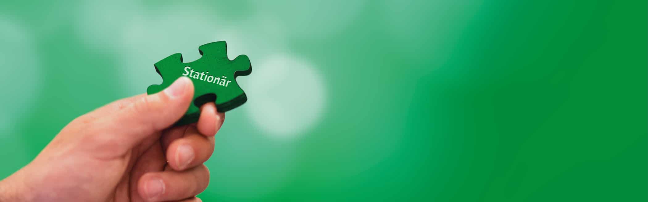 Hand hält ein grünes Puzzle mit der Aufschrift 'Stationär'