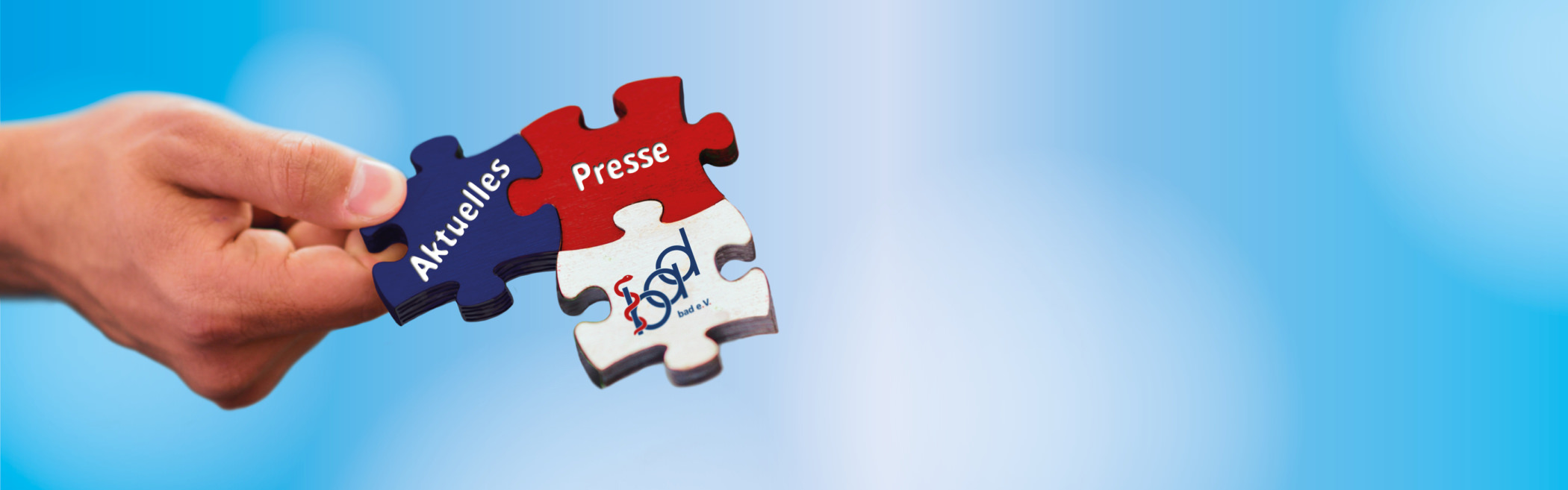 Bild eines Puzzles, das von einer Hand gehalten wird, mit einem blauen Himmel im Hintergrund. Die Puzzleteile sind rot, weiß und blau und tragen die Aufschriften 'Aktuelles' und 'Presse‘ sowie das Logo des bad e. V., das eine Verbindung zwischen den Elementen symbolisiert.