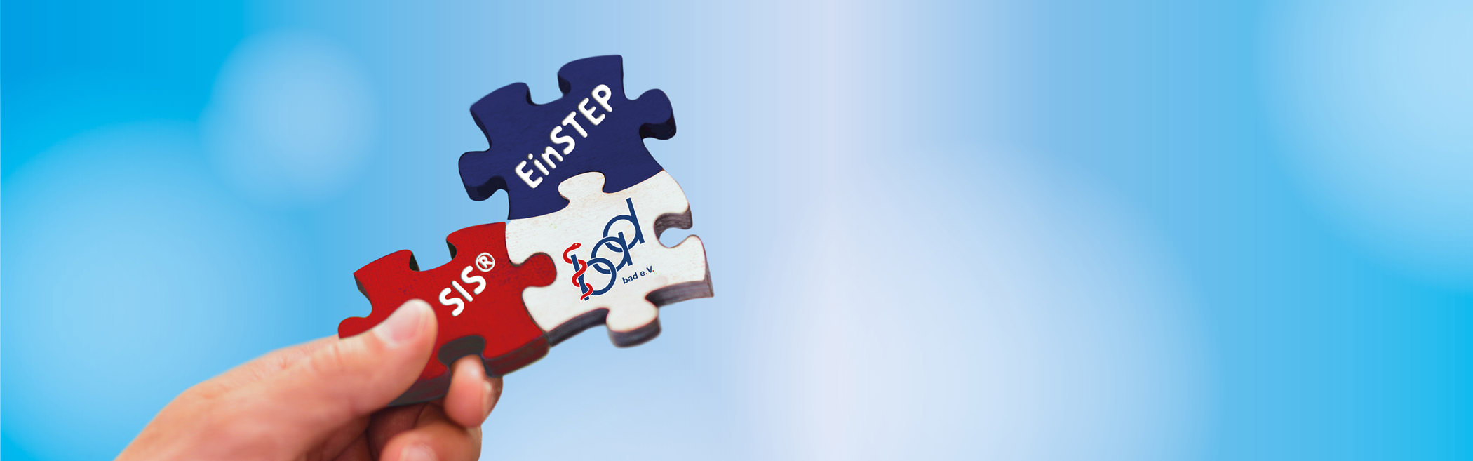 Bild eines Puzzles, das von einer Hand gehalten wird, mit einem blauen Himmel im Hintergrund. Die Puzzleteile sind rot, weiß und blau und tragen die Aufschriften 'EinSTEP' und 'SIS®' sowie das Logo des bad e. V., das eine Verbindung zwischen den Elementen symbolisiert.